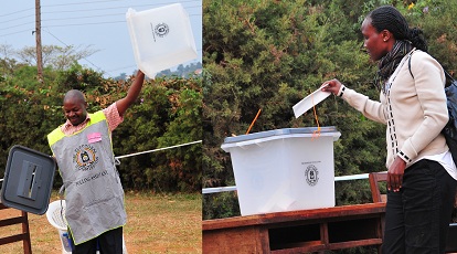 A polling assistant displays an empty box as a lady casts her vote